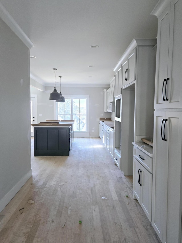 kitchen with white cabinetry, crown molding, decorative light fixtures, a kitchen island, and light hardwood / wood-style floors