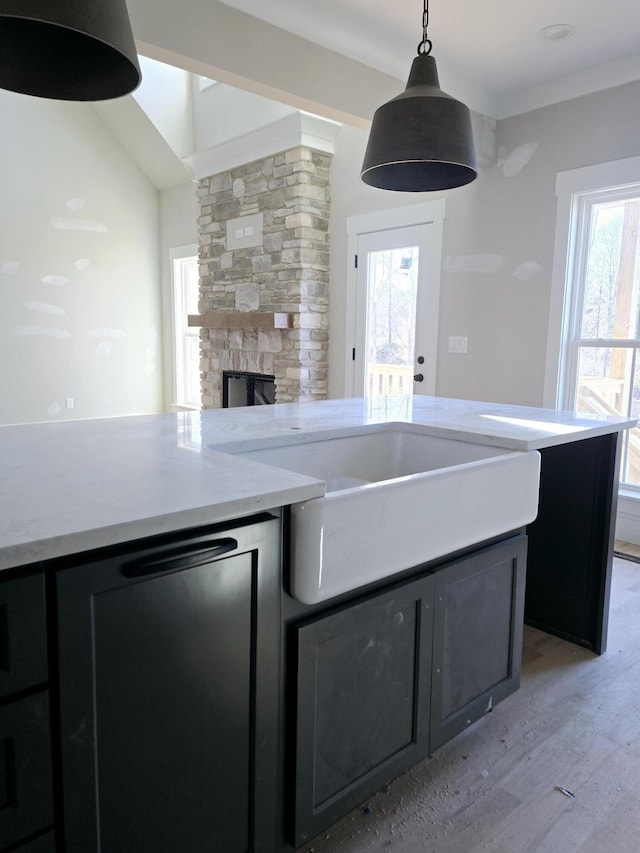 kitchen featuring a stone fireplace, sink, light stone counters, light hardwood / wood-style flooring, and pendant lighting