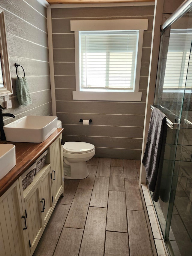 bathroom featuring toilet, wooden walls, a shower with shower door, and vanity