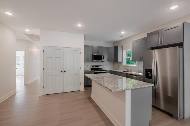 kitchen featuring a kitchen island, light stone counters, light wood-type flooring, stainless steel appliances, and gray cabinets