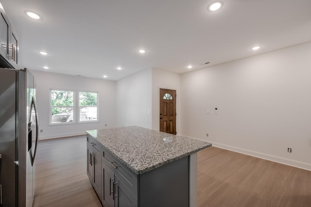 kitchen with light stone counters, gray cabinetry, a kitchen island, stainless steel fridge with ice dispenser, and light hardwood / wood-style floors