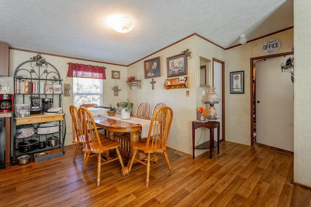 dining space featuring lofted ceiling, ornamental molding, hardwood / wood-style flooring, and a textured ceiling