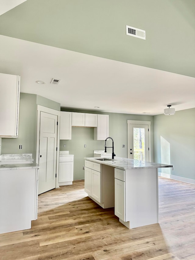 kitchen featuring white cabinets, a center island with sink, light hardwood / wood-style flooring, and sink