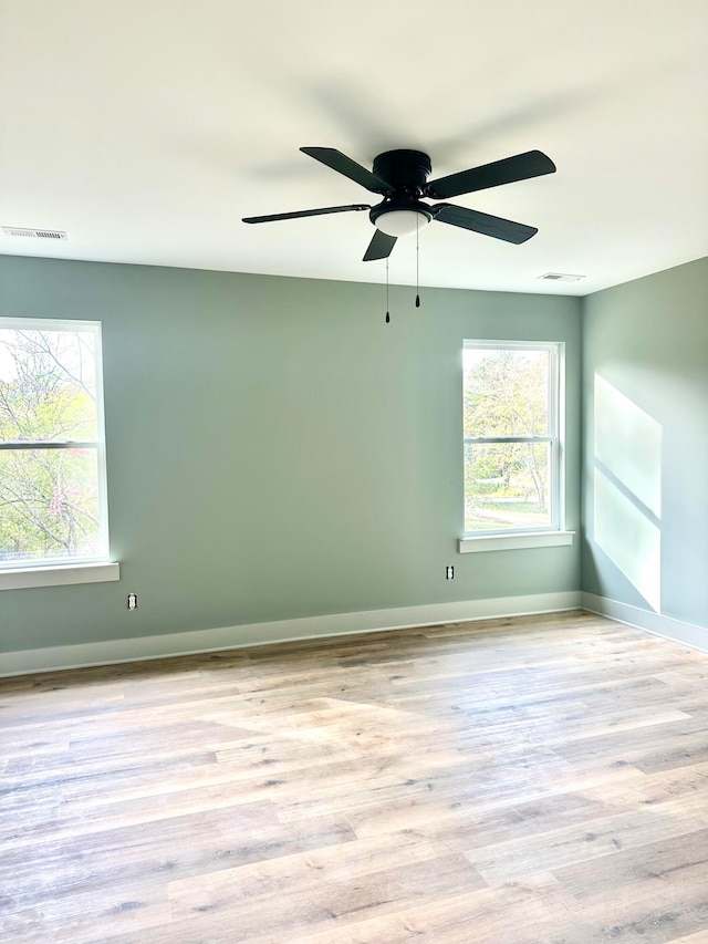 empty room with a wealth of natural light, ceiling fan, and light hardwood / wood-style floors