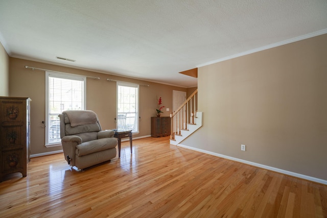 sitting room with stairs, light wood-style floors, visible vents, and ornamental molding