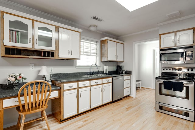 kitchen featuring dark countertops, crown molding, light wood-style flooring, stainless steel appliances, and a sink