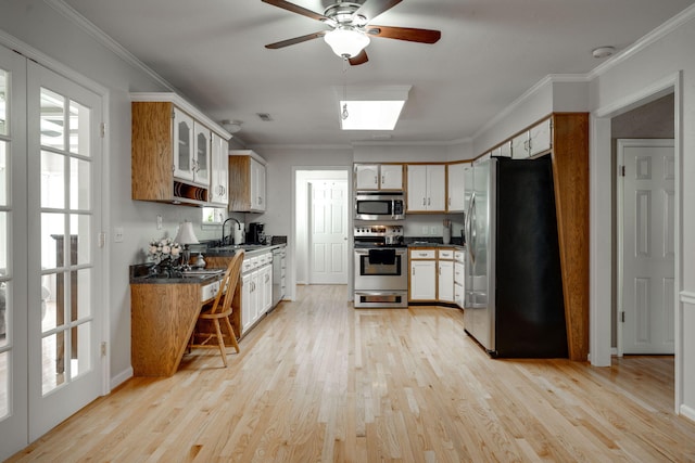 kitchen with dark countertops, stainless steel appliances, crown molding, light wood finished floors, and ceiling fan