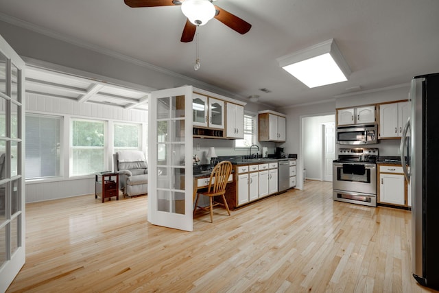 kitchen featuring light wood-style flooring, ornamental molding, a sink, dark countertops, and stainless steel appliances