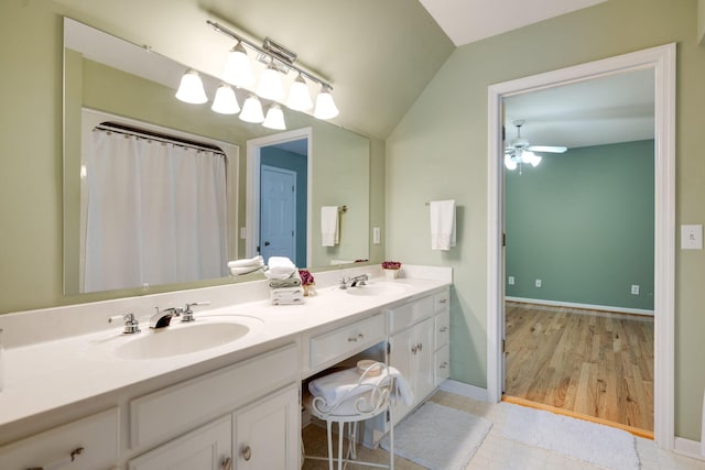 bathroom with baseboards, lofted ceiling, double vanity, a ceiling fan, and a sink