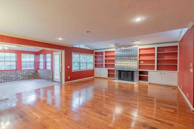 unfurnished living room with a textured ceiling, wooden walls, light wood-type flooring, and ceiling fan