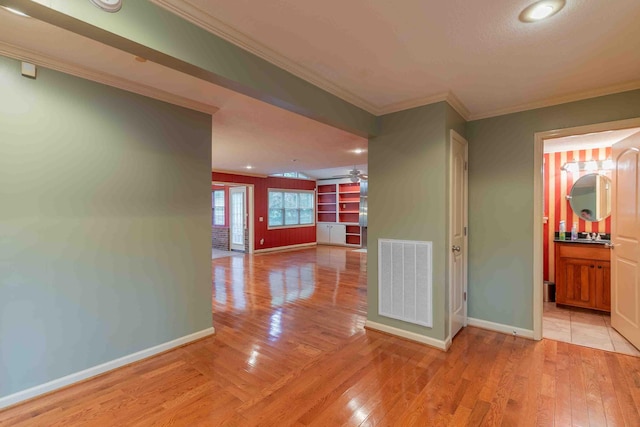 hall with crown molding, baseboards, visible vents, and light wood-style flooring