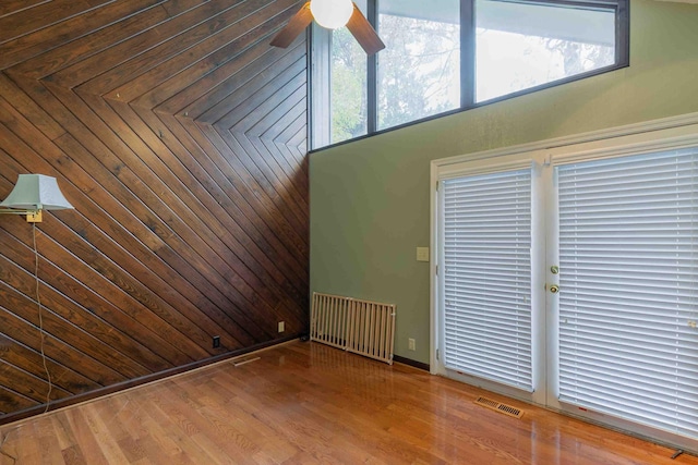 unfurnished room featuring wooden walls, hardwood / wood-style flooring, a healthy amount of sunlight, and ceiling fan