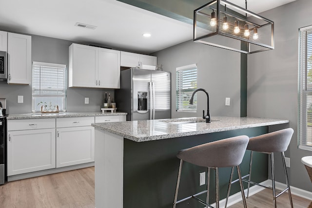 kitchen featuring white cabinets, hanging light fixtures, light hardwood / wood-style flooring, sink, and stainless steel appliances