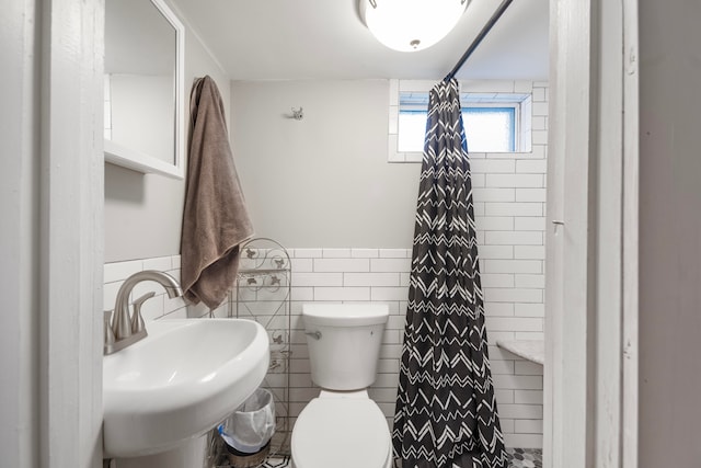 bathroom featuring toilet, curtained shower, sink, and tile walls