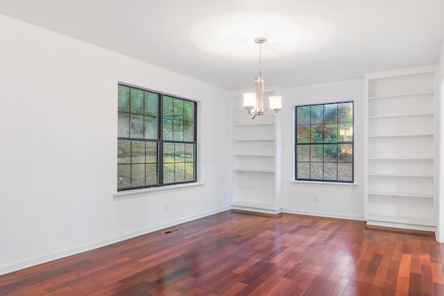 unfurnished dining area featuring built in shelves, dark hardwood / wood-style floors, and an inviting chandelier