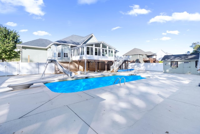 view of pool featuring a water slide, a patio, a sunroom, a shed, and a diving board