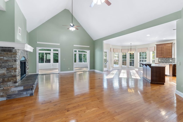 unfurnished living room with a stone fireplace, light hardwood / wood-style flooring, high vaulted ceiling, and plenty of natural light