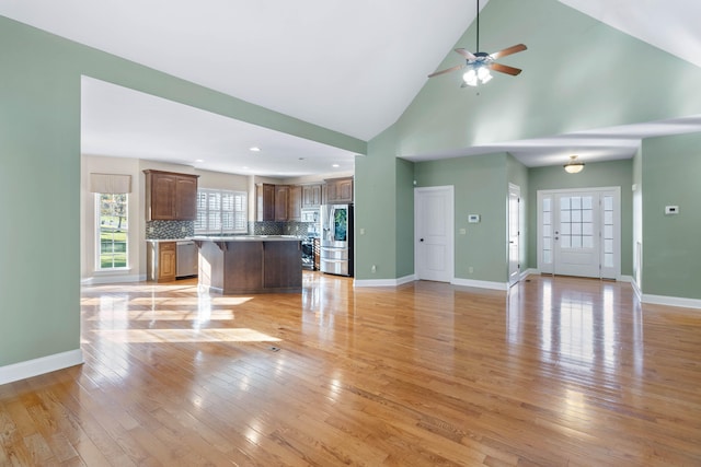 unfurnished living room with light hardwood / wood-style flooring, high vaulted ceiling, and ceiling fan