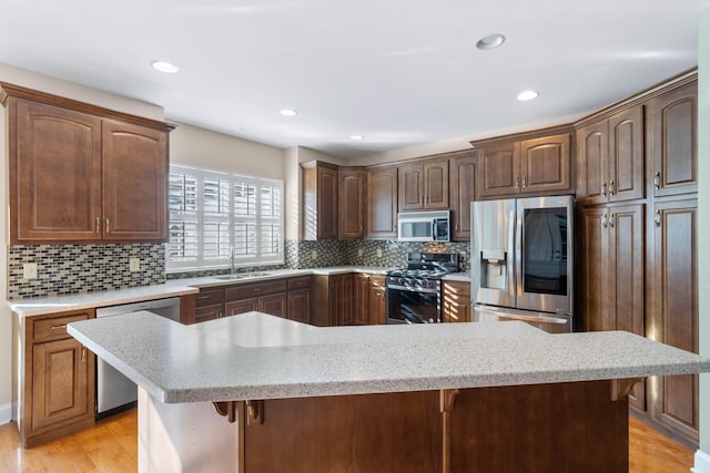 kitchen with sink, light wood-type flooring, backsplash, stainless steel appliances, and a breakfast bar area