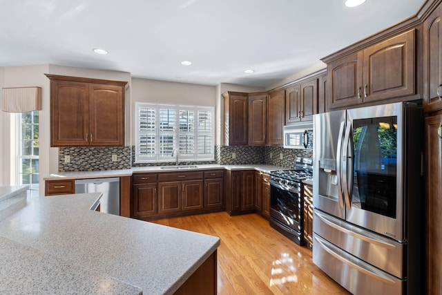 kitchen featuring backsplash, appliances with stainless steel finishes, light wood-type flooring, dark brown cabinetry, and sink