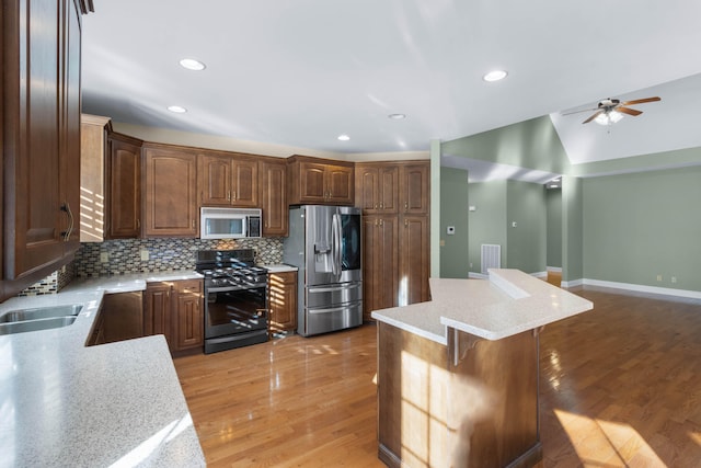 kitchen with appliances with stainless steel finishes, a kitchen bar, a kitchen island, backsplash, and hardwood / wood-style flooring