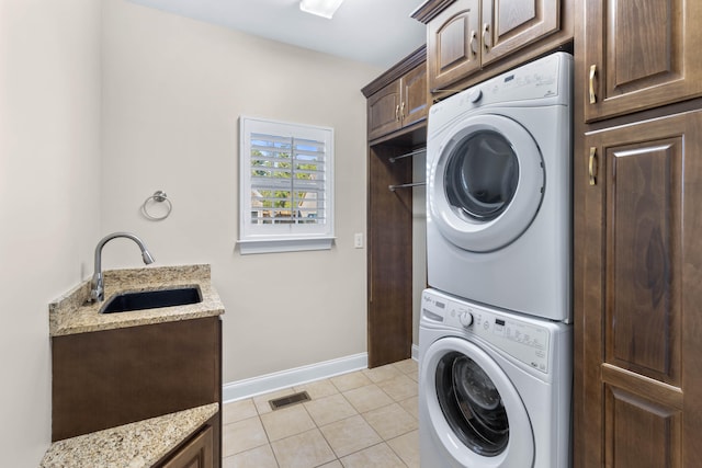 laundry area with sink, stacked washer and clothes dryer, cabinets, and light tile patterned floors