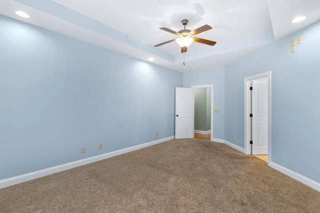 spare room with a tray ceiling, carpet, and ceiling fan