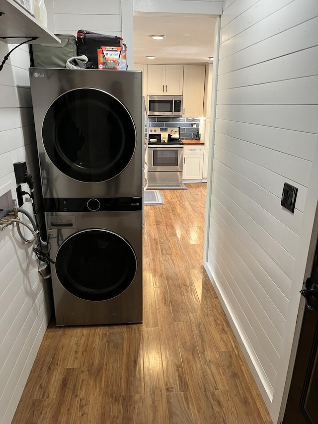 laundry room with stacked washer / drying machine and light hardwood / wood-style flooring