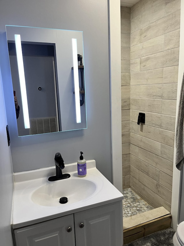 bathroom featuring toilet, vanity, and tiled shower