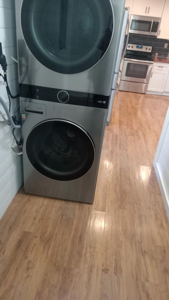 laundry area with stacked washer / drying machine and light wood-type flooring