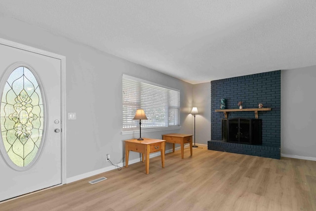 foyer entrance with a brick fireplace, a textured ceiling, and light hardwood / wood-style floors