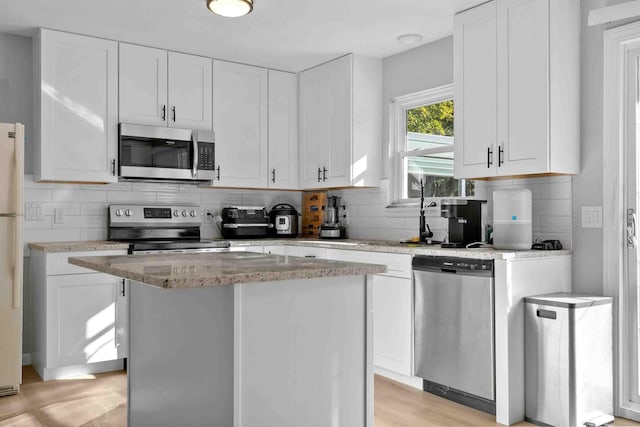 kitchen with stainless steel appliances, white cabinets, a kitchen island, and light wood-type flooring