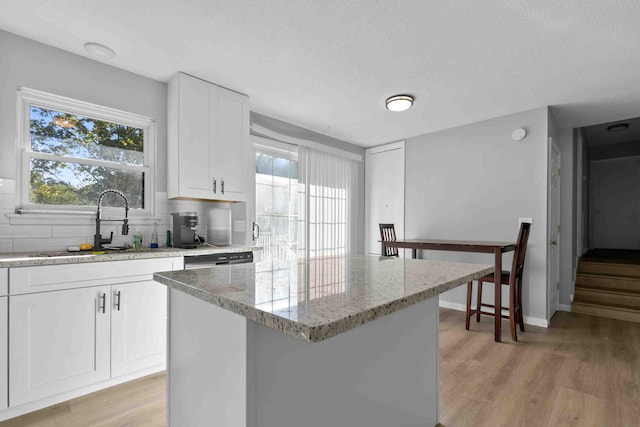 kitchen with light stone countertops, backsplash, a kitchen island, and white cabinetry