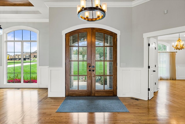 foyer entrance with hardwood / wood-style floors, an inviting chandelier, ornamental molding, and french doors