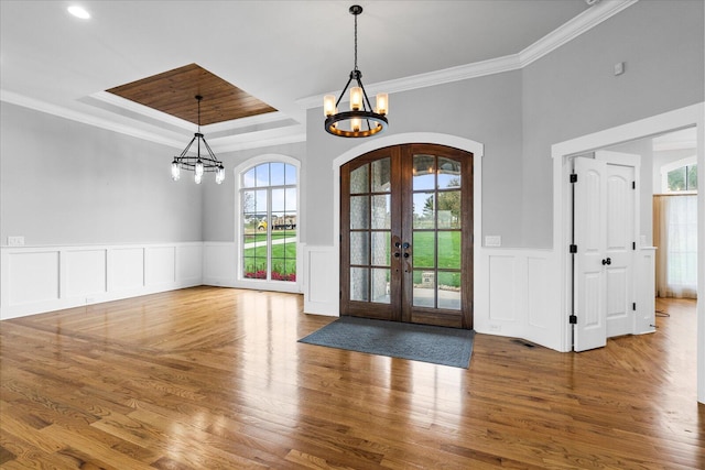 entrance foyer featuring hardwood / wood-style flooring, an inviting chandelier, crown molding, and french doors