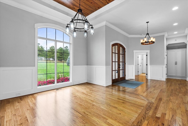 unfurnished dining area with crown molding, french doors, a chandelier, and light wood-type flooring