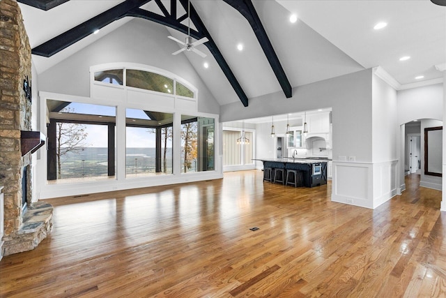 unfurnished living room with ceiling fan, beamed ceiling, high vaulted ceiling, and light wood-type flooring