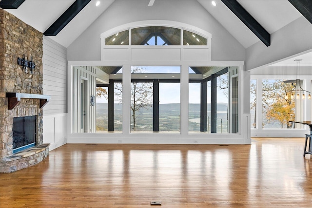 unfurnished living room with plenty of natural light, a stone fireplace, wood-type flooring, and high vaulted ceiling