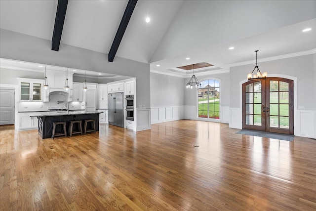 unfurnished living room with french doors, sink, ornamental molding, light wood-type flooring, and beam ceiling