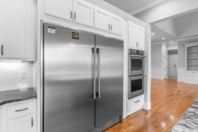 kitchen featuring decorative backsplash, appliances with stainless steel finishes, light wood-type flooring, dark stone counters, and white cabinets