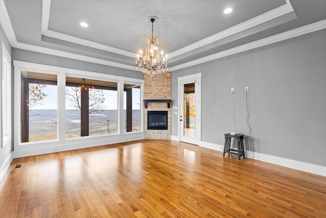 unfurnished living room with a raised ceiling, wood-type flooring, a fireplace, and a chandelier