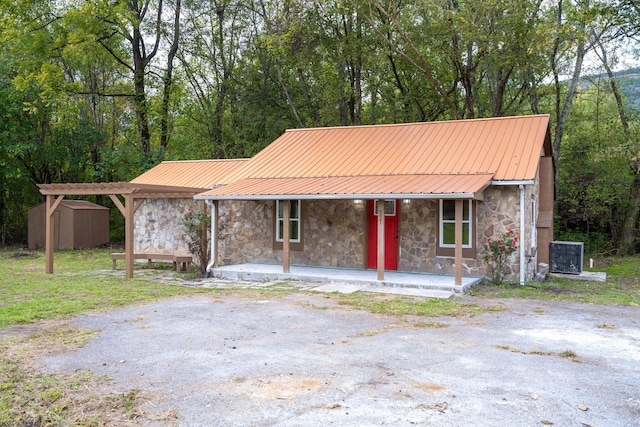 view of front of property featuring a porch, a storage shed, and central AC