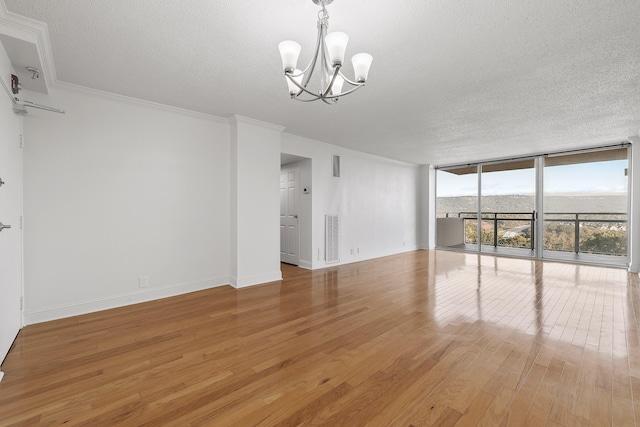 unfurnished living room with a textured ceiling, a chandelier, wood-type flooring, crown molding, and a wall of windows