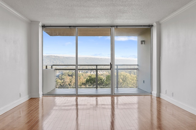 empty room with a mountain view, ornamental molding, a wall of windows, and light hardwood / wood-style floors