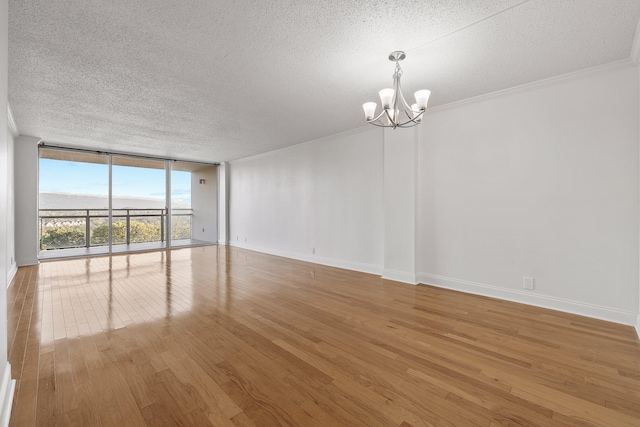 unfurnished room featuring hardwood / wood-style floors, a textured ceiling, a chandelier, floor to ceiling windows, and ornamental molding