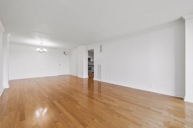 empty room featuring ornamental molding, light hardwood / wood-style flooring, a notable chandelier, and a textured ceiling