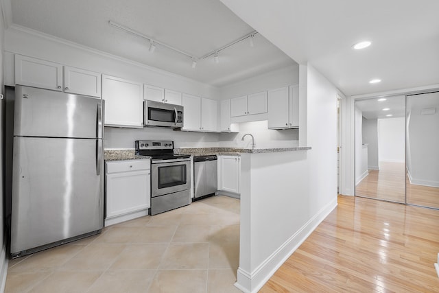 kitchen featuring track lighting, stainless steel appliances, dark stone countertops, white cabinets, and light hardwood / wood-style floors