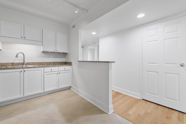 kitchen with sink, white cabinetry, rail lighting, and dark stone counters