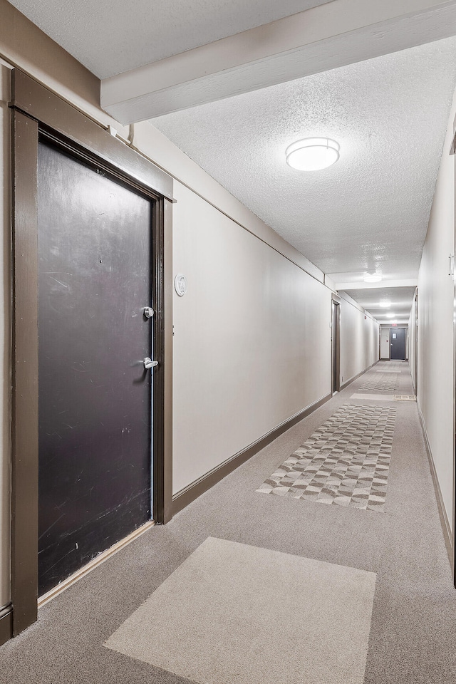 hall with beam ceiling, a textured ceiling, and carpet flooring