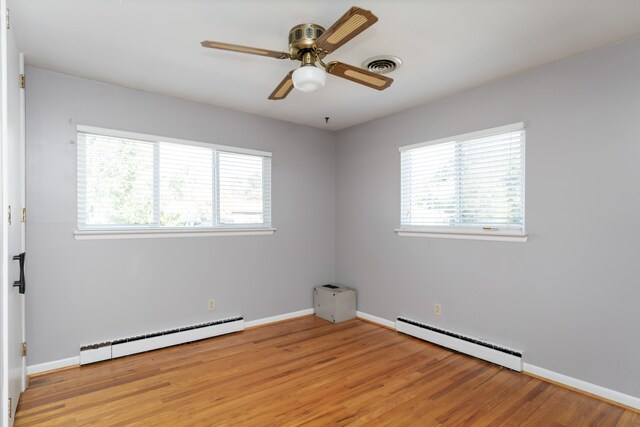 spare room with light hardwood / wood-style floors, a baseboard heating unit, and a healthy amount of sunlight